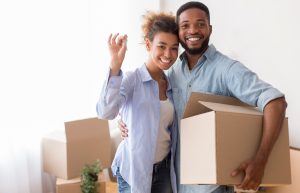 Couple Showing Key Holding Moving Box Standing In New Home